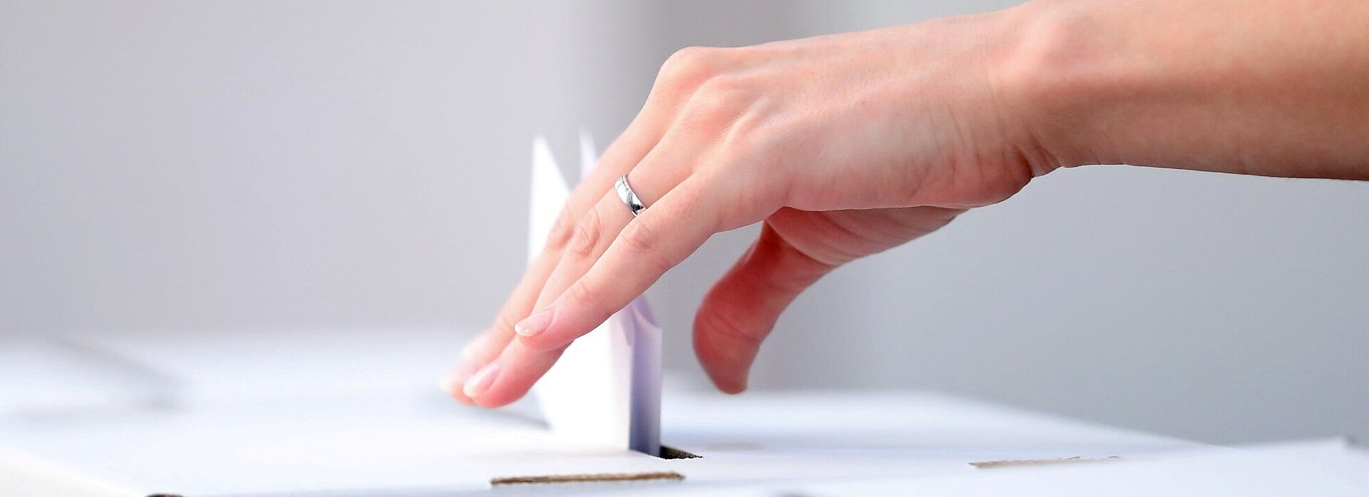 Detailaufnahme einer Hand, die einen Wahlschein einwirft