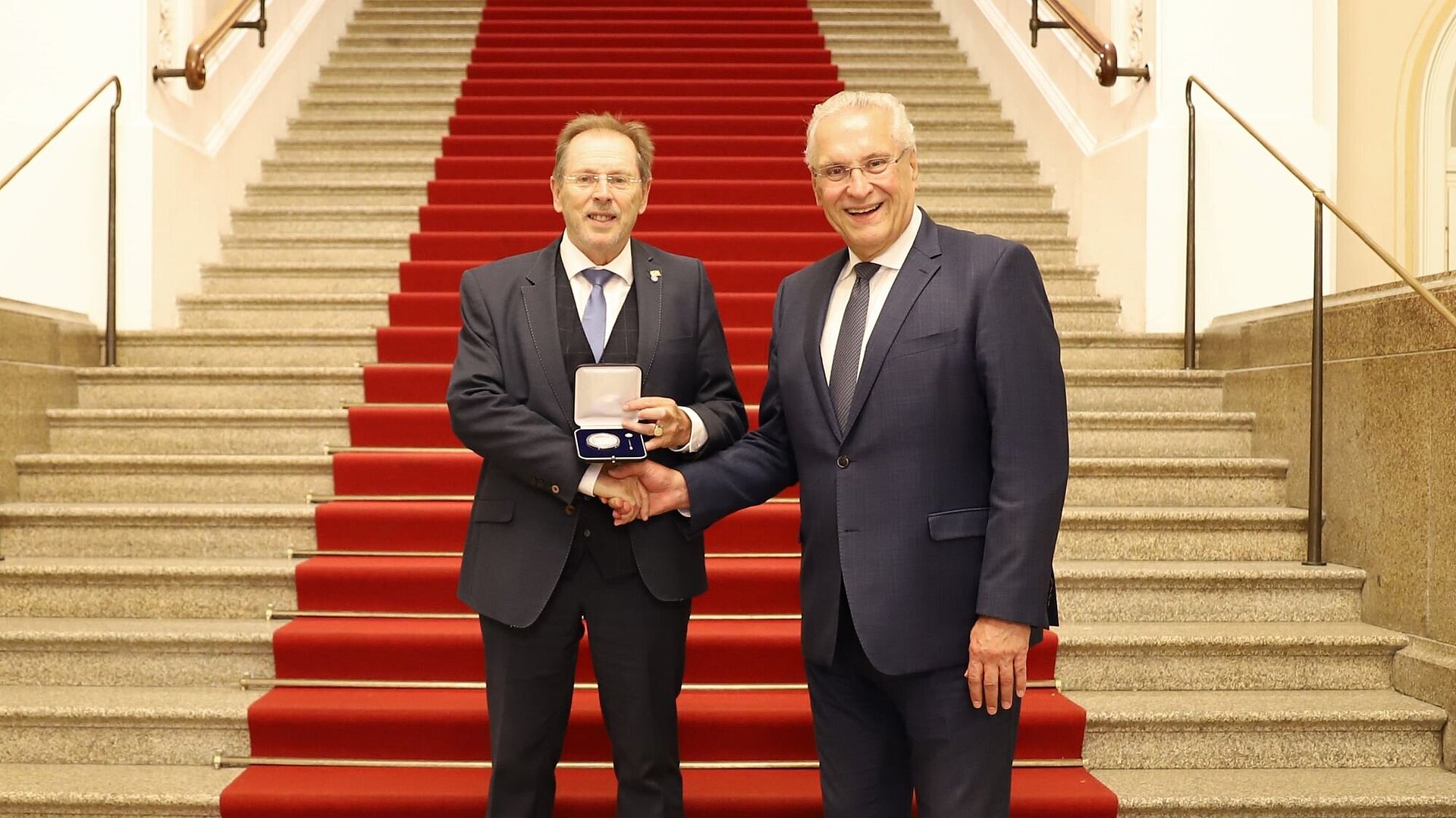 Auf dem Bild sind Innenminister Joachim Herrmann und der mit der Kommunalen Verdienstmedaille in Silber ausgezeichnete Hans Herold im Bayerischen Landtag bei der Ordensübergabe zu sehen.