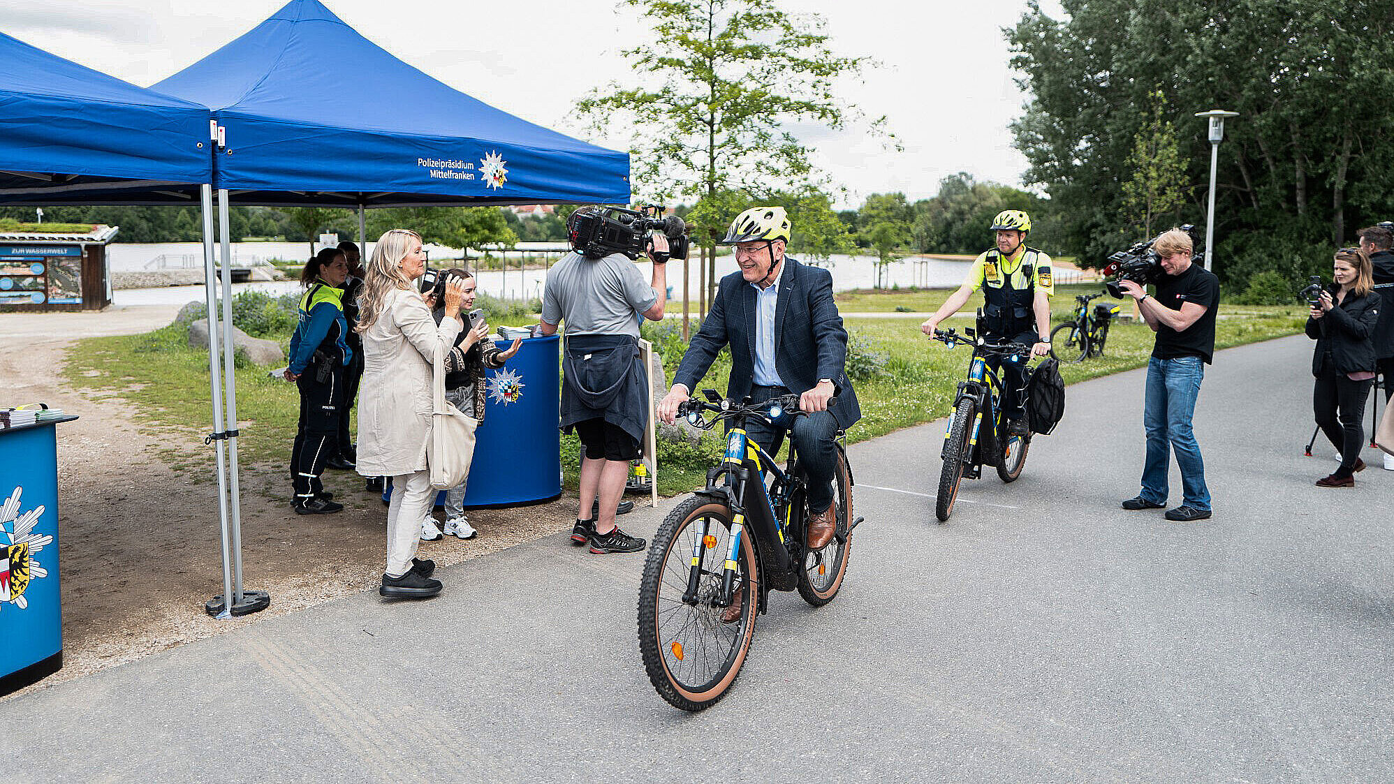 Innenminister Joachim Herrmann fährt auf einem Polizeifahrrad am Polizeikontrollstand vorbei