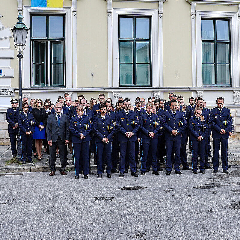 Polizisten stehen in einer Gruppe zwischen zwei Streifenwagen vor dem Eingang des Bayerischen Innenministeriums und halten eine Schweigeminute.