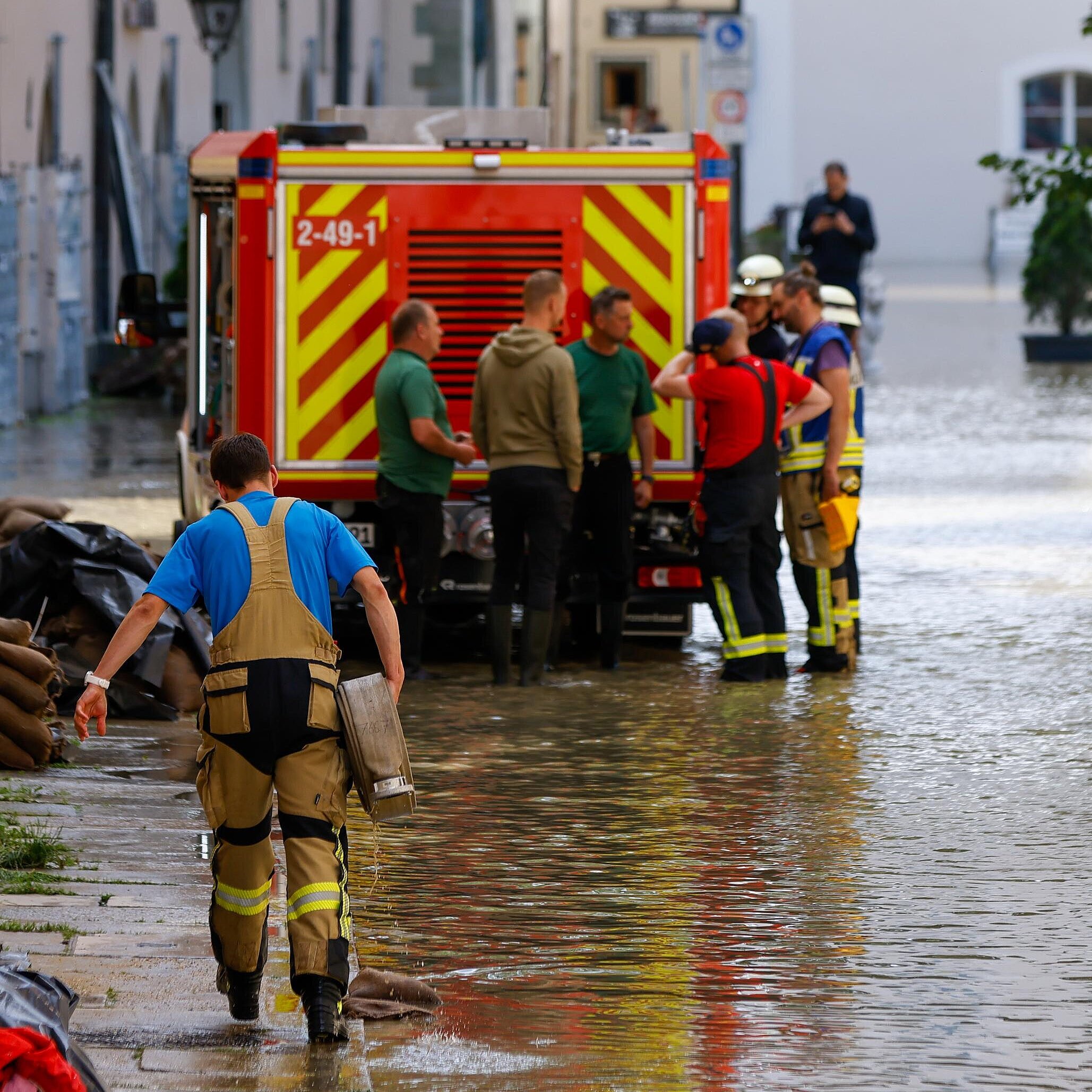 Einsatzkräfte in Stadt mit Hochwasser bei der Arbeit, im Hintergrund ein Einsatzfahrzeug