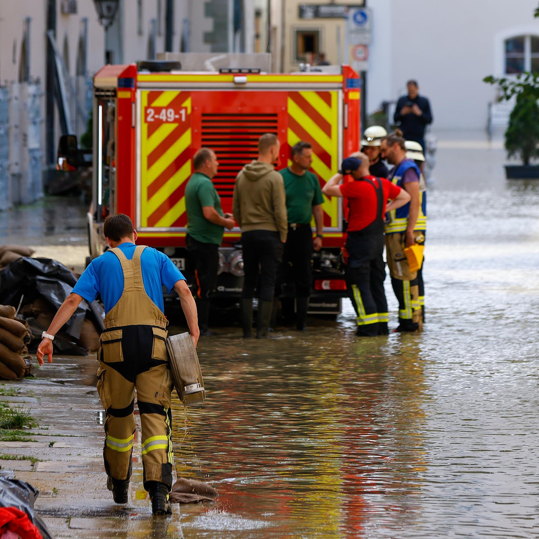 Einsatzkräfte in Stadt mit Hochwasser bei der Arbeit, im Hintergrund ein Einsatzfahrzeug