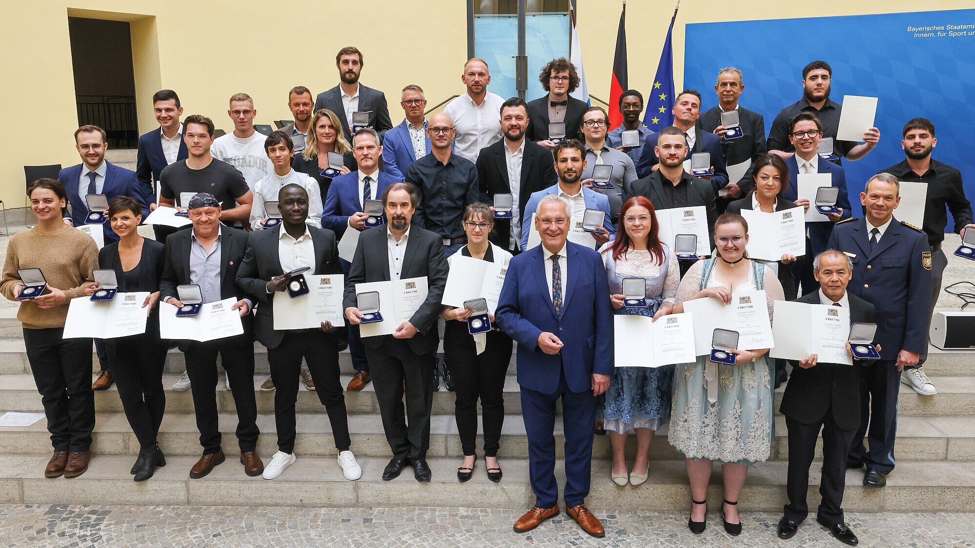 Auf dem Bild sind Herr Staatsminister Joachim Herrmann sowie Landespolizeipräsident Michael Schwald mit den mit der "Courage-Medaille" ausgezeichneten Personen zu sehen.