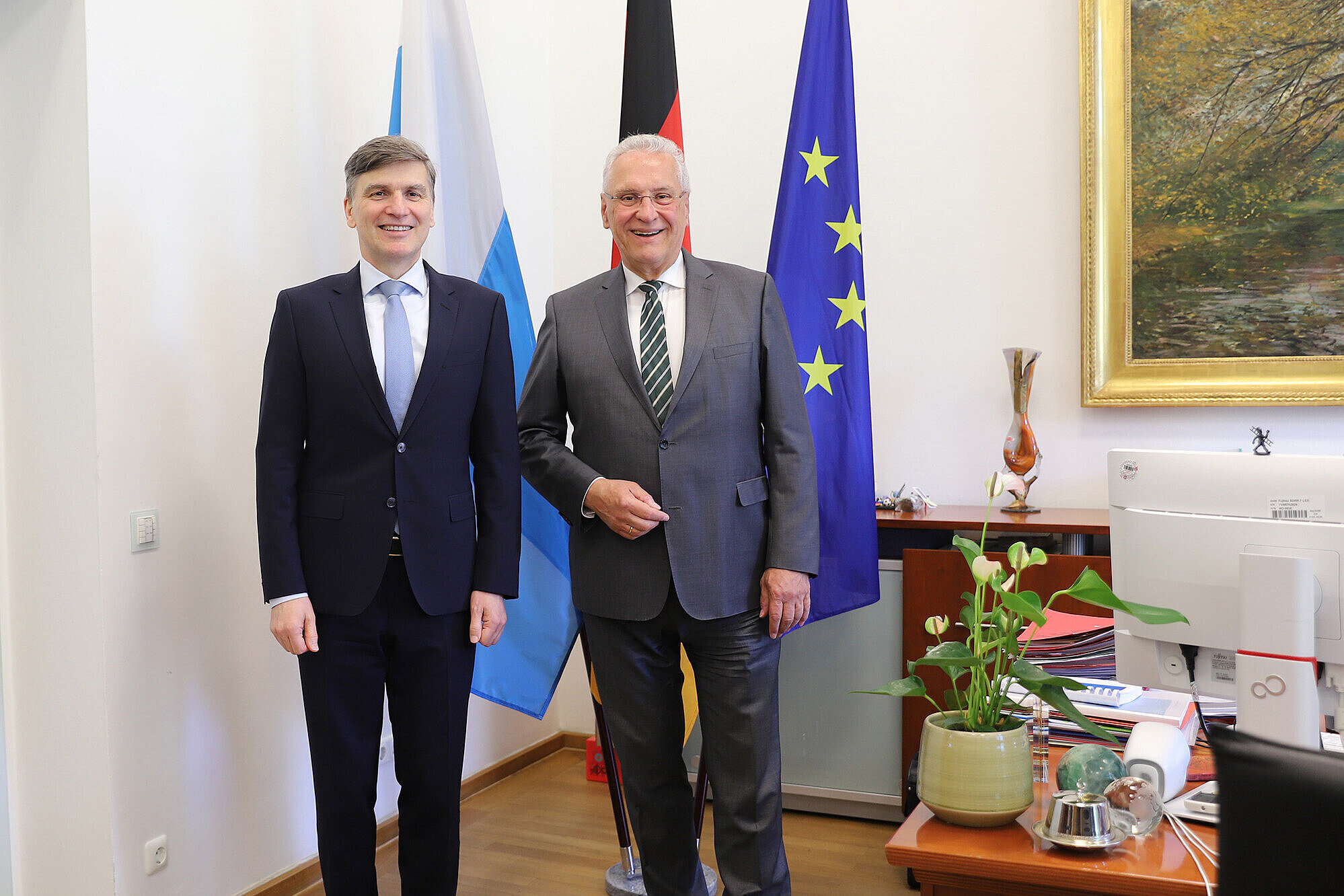 Auf dem Bild links Botschafter Marián Jakubócy, rechts Innenminister Joachim Herrmann vor Fahnenset in Büro