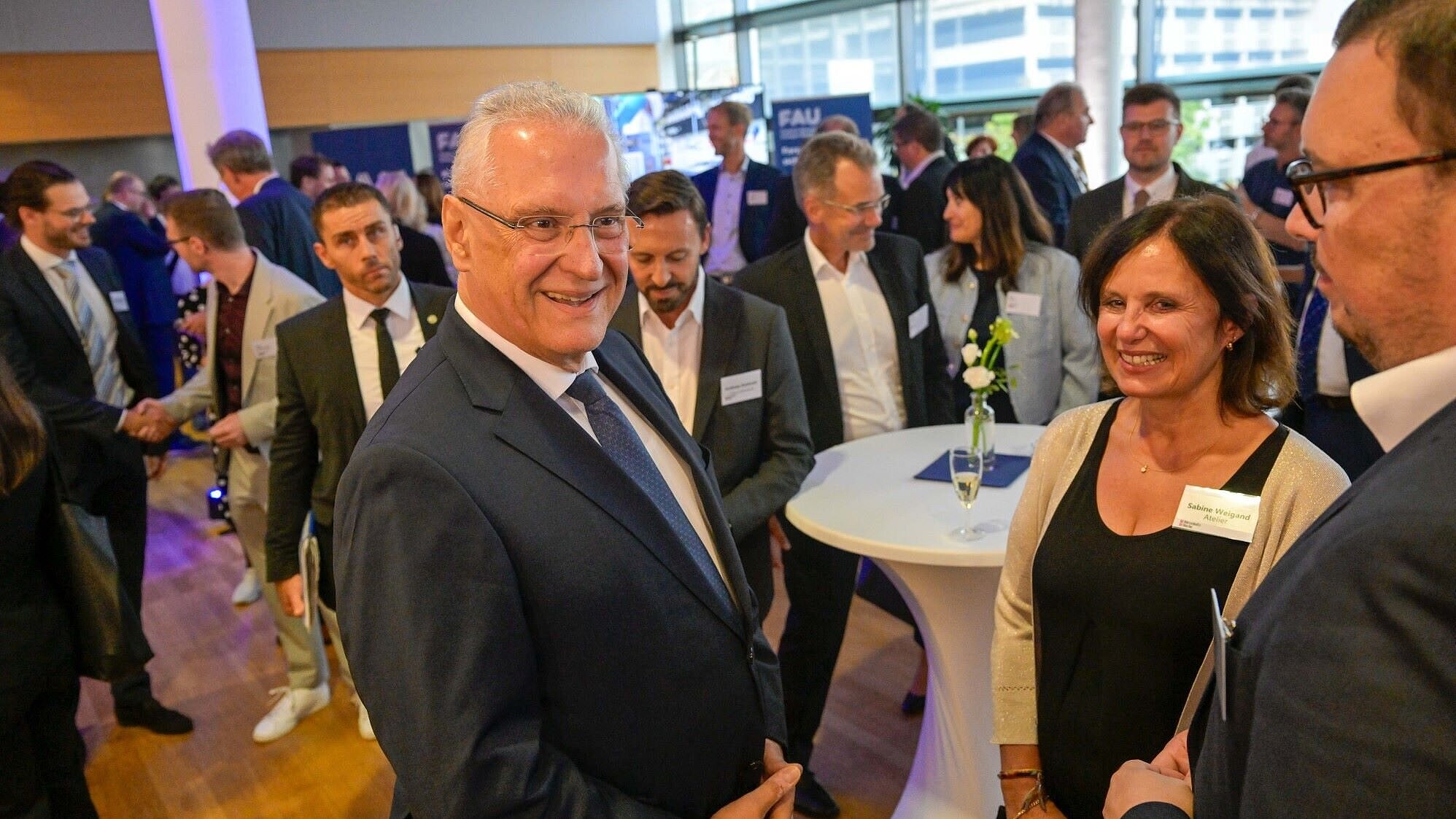 Auf dem Bild ist Innenminister Joachim Herrmann im Gespräch mit Teilnehmerinnen und Teilnehmern des Staatsempfangs anlässlich des "Innovation Day" zu sehen.