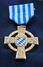 Steckkreuz der Feuerwehr in Gold mit blau-weiß gestreiftem Band auf einer schwarzen Decke liegend