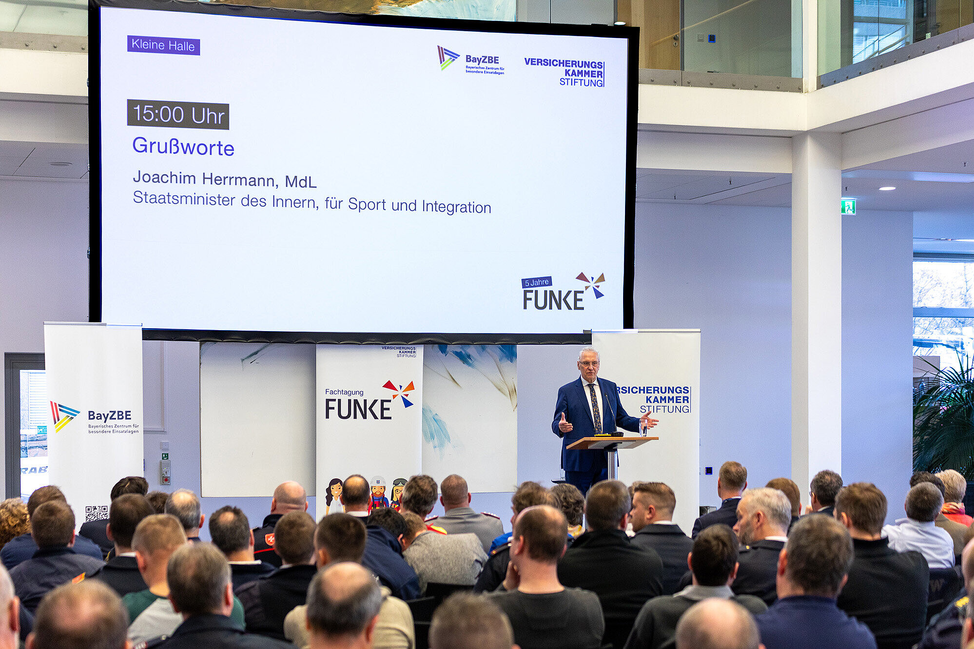auf dem Bild Innenminister Joachim Herrmann auf der Bühne am Rednerpult bei seinem Grußwort an die Gäste der Fachtagung