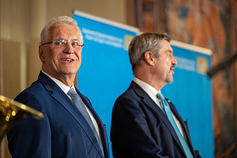 links Innenminister Joachim Herrmann, rechts Ministerpräsident Dr. Markus Söder vor einer blauen Pressewand in der Münchner Residenz
