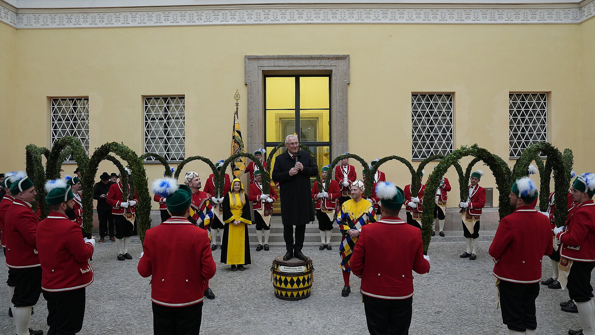 Innenminister Joachim Herrmann bei Show der Schäffler in der Mitte auf einem Fass stehend, hält eine Ansprache. Um ihn herum die Schäffler im traditionellen Gewand.