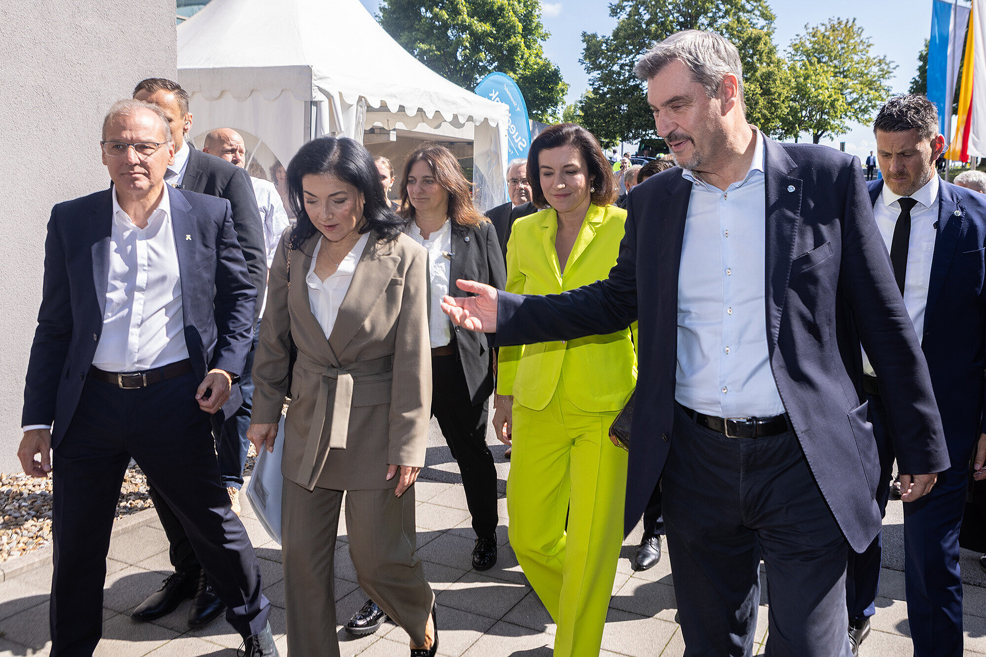 Gruppe von Personen (rechts Dr. Markus Söder) im Gespräch bei einer Veranstaltung im Freien, einige tragen formelle Kleidung, eine Person trägt eine leuchtend gelbe Jacke