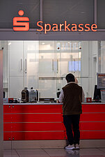 Eine Person wartet am roten Sparkassenschalter mit dem Logo der Sparkasse