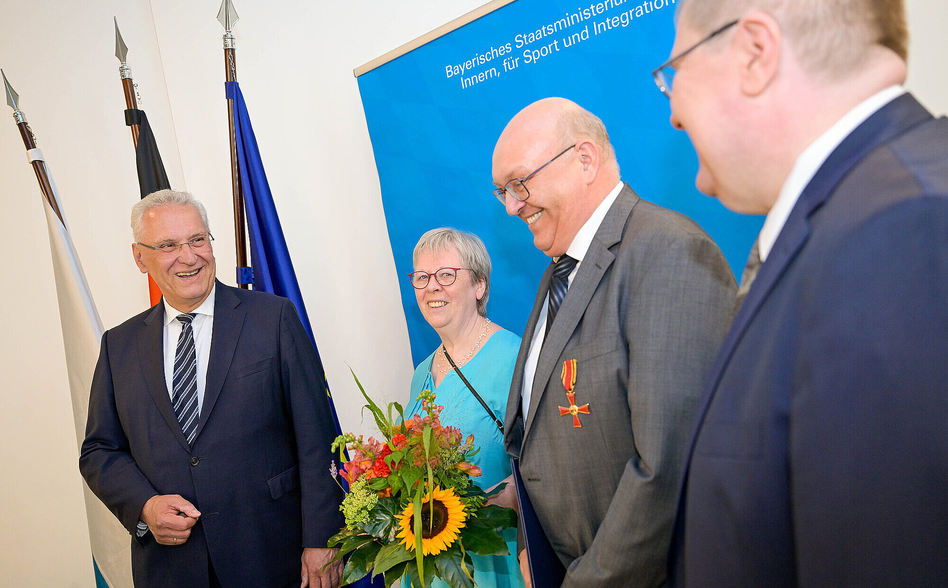 Herrmann neben Geehrten mit Blumenstrauß und Verdienstkreuznadel