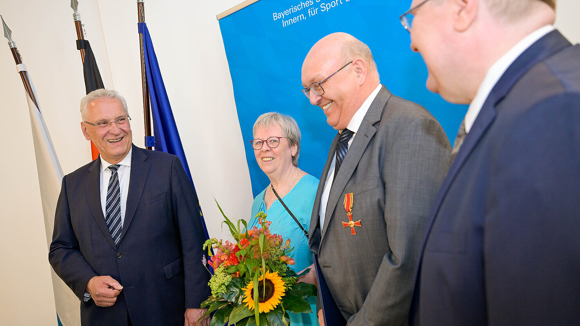 Herrmann neben Geehrten mit Blumenstrauß und Verdienstkreuznadel