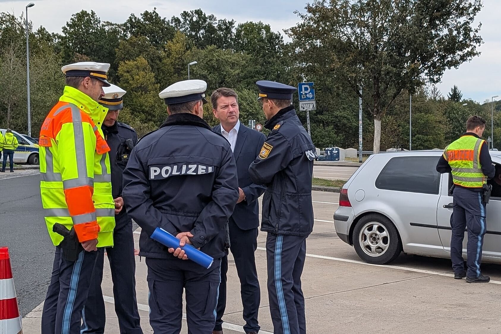 Innenstaatssekretär Kirchner unterhält sich mit mehreren Polizisten auf einem Parkplatz. Hinter ihnen hat ein Polizeibeamter ein Fahrzeug angehalten.