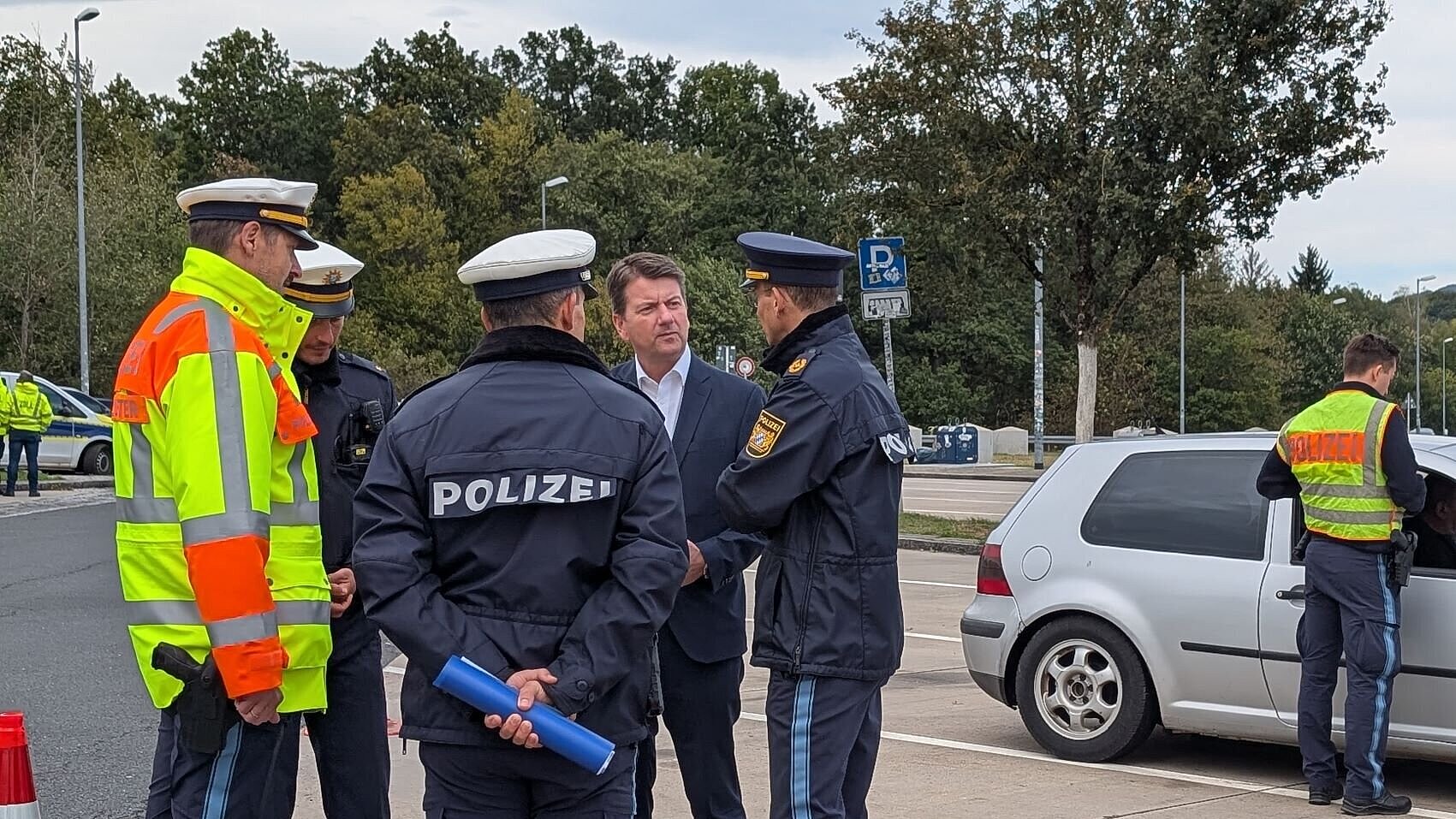 Innenstaatssekretär Kirchner unterhält sich mit mehreren Polizisten auf einem Parkplatz. Hinter ihnen hat ein Polizeibeamter ein Fahrzeug angehalten.