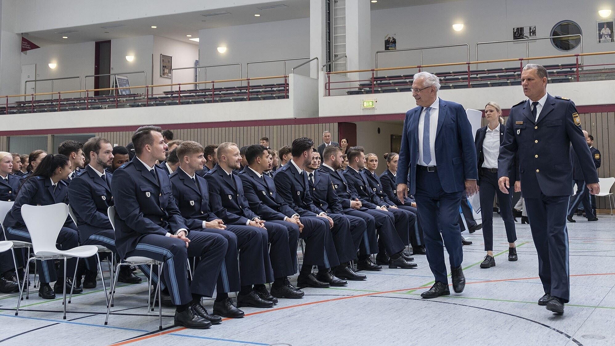Auf dem Bild ist Innenminister Joachim Herrmann zu sehen, wie er sitzenden Polizisten und Polizistinnen bei der Veranstaltung anlässlich der Begrüßung der neuen Polizeibeschäftigten zulächelt.