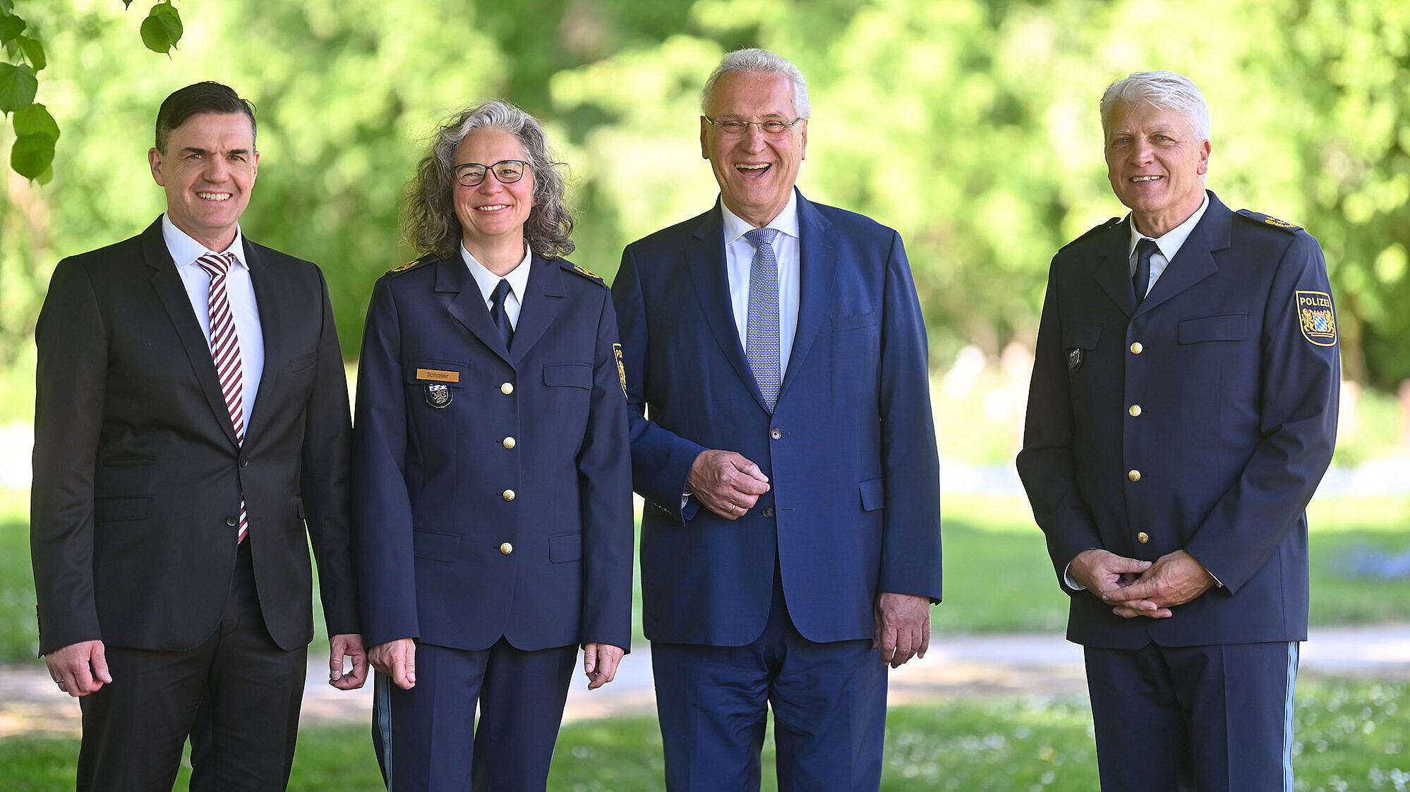 Gruppenbild (von links nach rechts:) Dirk Schmidt, neuer Polizeivizepräsident PP Oberbayern Nord, Kerstin Schaller, neue Polizeipräsidentin PP Oberbayern Nord, Innenminister Joachim Herrmann, Günther Gietl Polizeipräsident Oberbayern Nord a.D. im Hintergrund grüne Bäume