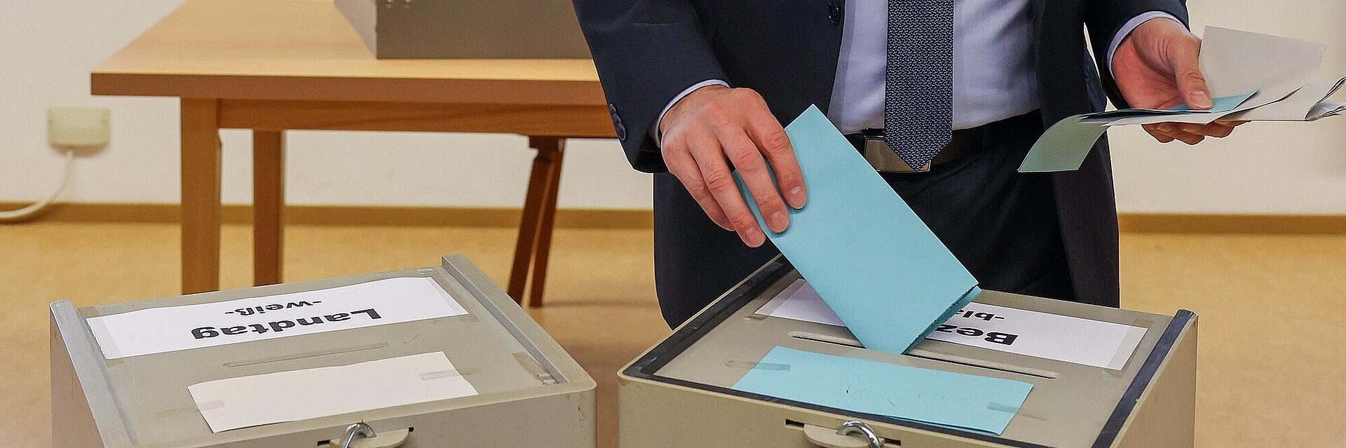 Eine Person die einen Wahlzettel in eine von zwei Wahlurnen einwirft