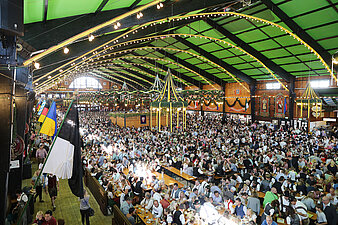 Wiesnzelt von Innen mit Sicht von oben herab auf die Bierbänke mit vielen Besuchern
