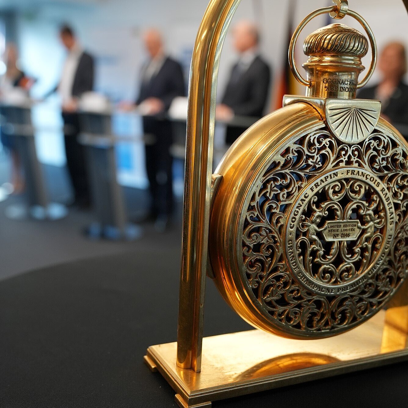 auf dem Bild: goldene Luxusuhr im Vordergrund im Hintergrund Pressekonferenz