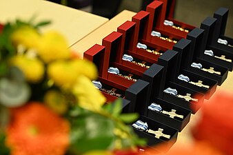 Steckkreuze in Gold und Silber in geöffneten schwarzen und roten Etuis auf einem Tisch liegend, daneben ein Blumenstrauß