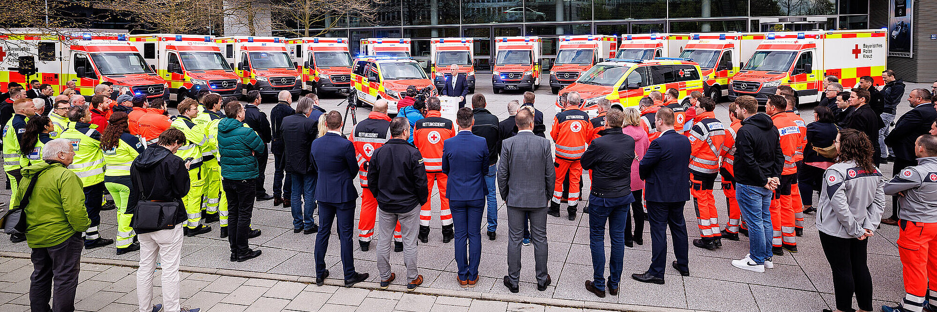 Rede von Innenminister Herrmann vor dem Mercedes-Benz Gebäude, hinter ihm sind mehrere Rettungsfahrzeuge für das BRK im Halbkreis aufgereiht