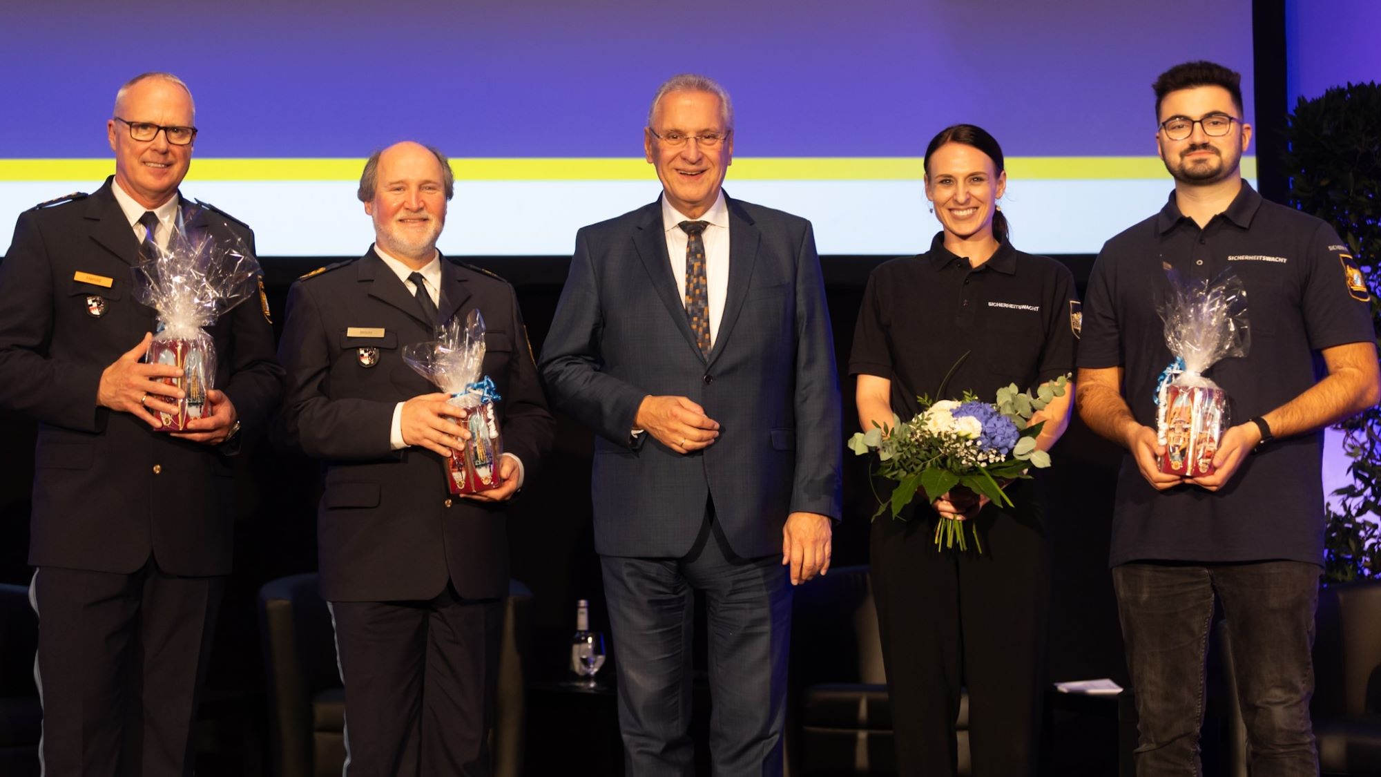 Auf dem Bild ist Innenminister Joachim Herrmann zu sehen, umringt von vier Personen, die für ihr Engagement geehrt wurden.